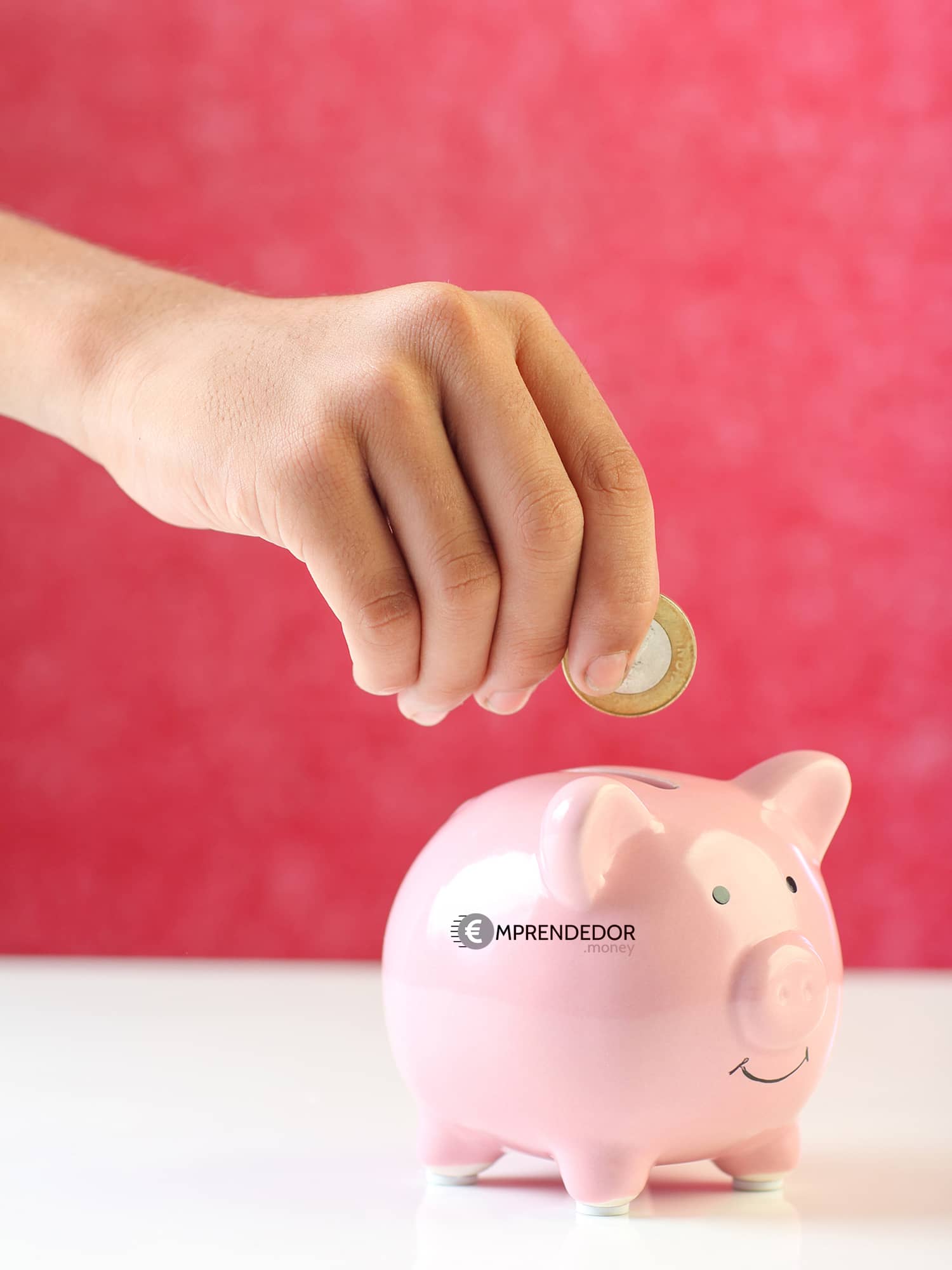 Mano depositando una moneda en una alcancía de cerdito, simbolizando el ahorro para un bebé.