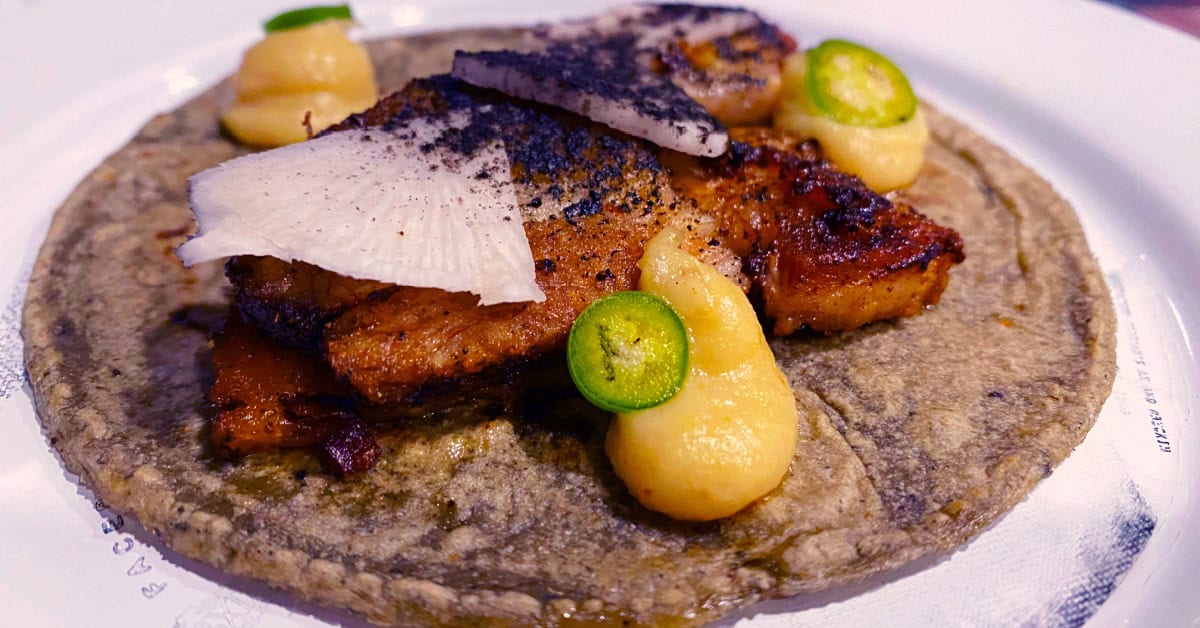 Tacos made with porky belly, confit garlic puree, pickled black radish, serrano pepper slices, and tortilla ash at Tizne Tacomotora in Mexico City