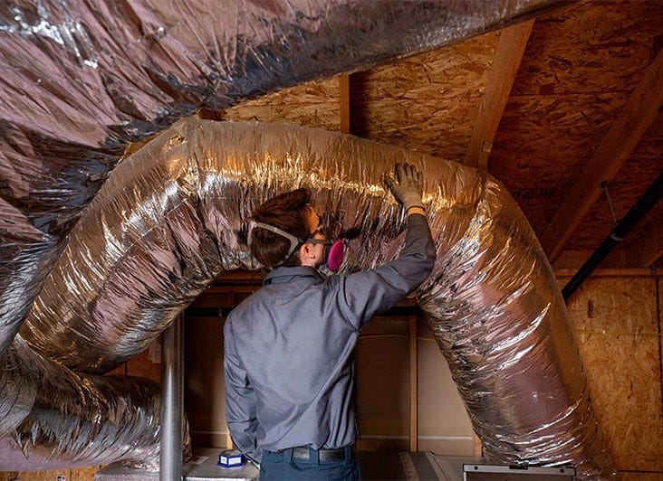 A friendly technician from Fetch‑A‑Tech, equipped with safety gear, carefully inspects large insulated air ducts in a wooden attic space. Our team takes pride in providing honest, helpful service to keep Las Vegas businesses comfortable and running smoothly.