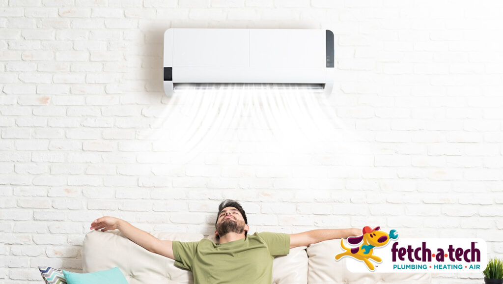 A man enjoys relaxing on his couch as cool, refreshing air flows from a wall-mounted air conditioner. The Fetch‑A‑Tech logo in the corner shows this is a family-owned Las Vegas company dedicated to keeping your home comfortable with honest, helpful service.