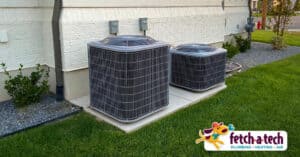 Two outdoor air conditioning units neatly installed on a concrete pad beside a home, surrounded by well-kept grass and shrubs in Las Vegas. The Fetch‑A‑Tech Plumbing, Heating, and Air logo appears in the bottom right corner, reflecting our family-owned commitment to comfort and reliable service for your home.
