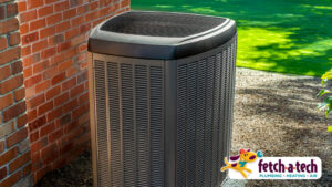 A central air conditioning unit sits neatly outside a Las Vegas home beside a brick wall, surrounded by green grass and bathed in warm sunlight—ready to keep your family comfortable. The Fetch‑A‑Tech logo appears in the lower right, representing our honest, family-owned service dedicated to helping our neighbors stay cool all summer long.