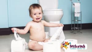 A happy baby sits on a bathroom floor in Las Vegas, playfully unrolling toilet paper with several rolls scattered nearby. A toilet and holder are seen in the background, along with the Fetch‑A‑Tech logo—highlighting our family-owned team’s commitment to keeping your home comfortable, tidy, and ready for every joyful moment.