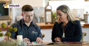 A friendly Fetch‑A‑Tech technician, Romo, sits with a customer at her kitchen table in Las Vegas, reviewing important documents together. Both are focused and comfortable, reflecting the helpful and trustworthy service that comes from a local, family-owned company.