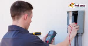 A Fetch‑A‑Tech technician carefully tests an electrical panel with a digital multimeter outside a Las Vegas home, ensuring safety and comfort for your family. The trusted Fetch‑A‑Tech logo is displayed in the top right, highlighting our commitment to friendly, reliable service in the Las Vegas community.