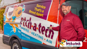 A friendly Fetch‑A‑Tech technician, dressed in a maroon shirt and cap, stands next to a brightly wrapped service van featuring plumbing, heating, and air services. The scene highlights Fetch‑A‑Tech’s helpful team and commitment to comfort for Las Vegas families.