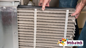 A helpful technician replaces a dirty HVAC air filter with a fresh, clean one, ensuring comfort for a Las Vegas home. The Fetch-A-Tech Plumbing, Heating, Air logo in the bottom right corner highlights the family-owned service’s commitment to honest and reliable care.