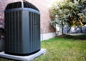 A reliable outdoor air conditioning unit is installed on a sturdy concrete pad beside a brick home in Las Vegas, surrounded by green grass and a shady tree—providing comfort and peace of mind for the whole family with help from your local Fetch‑A‑Tech team.