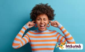 A woman in a striped shirt covers her ears and squints, looking uncomfortable against a blue background. The Fetch‑A‑Tech logo appears in the bottom right corner, representing our friendly, family-owned team dedicated to helping Las Vegas families find relief from noisy home issues.