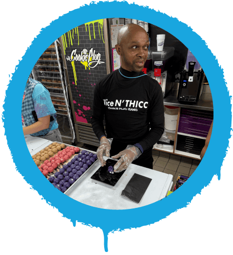 Team worker rolling out purple and pink cookie dough in a cookie shop.