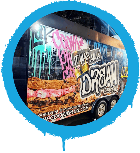 Food truck with colorful graffiti along the side that says 'Cookie Plug' and 'It was all a dream' with a golden crown on top with large cookies in the background.