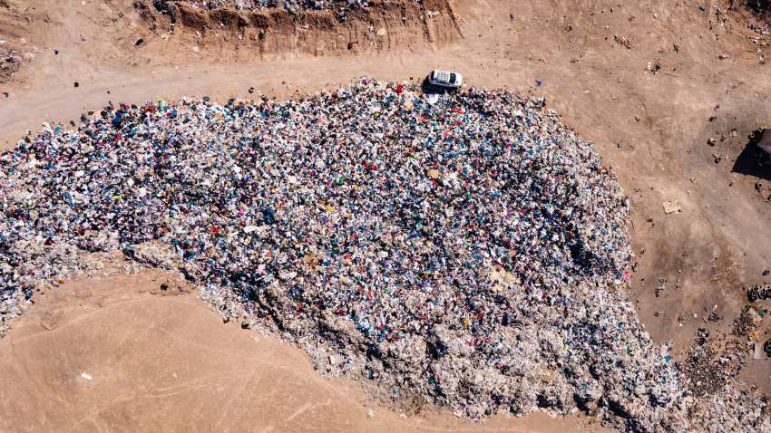 Aerial view of clothing waste dump with a car dwarfed by a huge pile of clothes