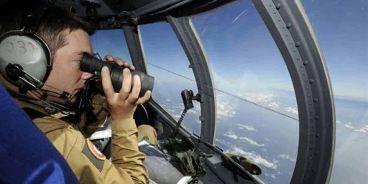 A pilot looking out the window through a pair of binoculars