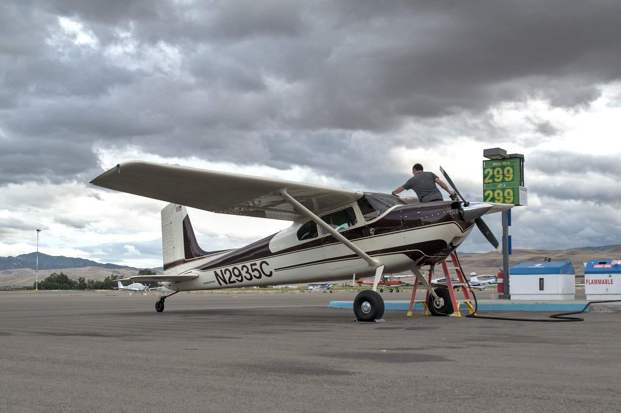 A man on top of a white and purple Cessna 180 plane on the runway
