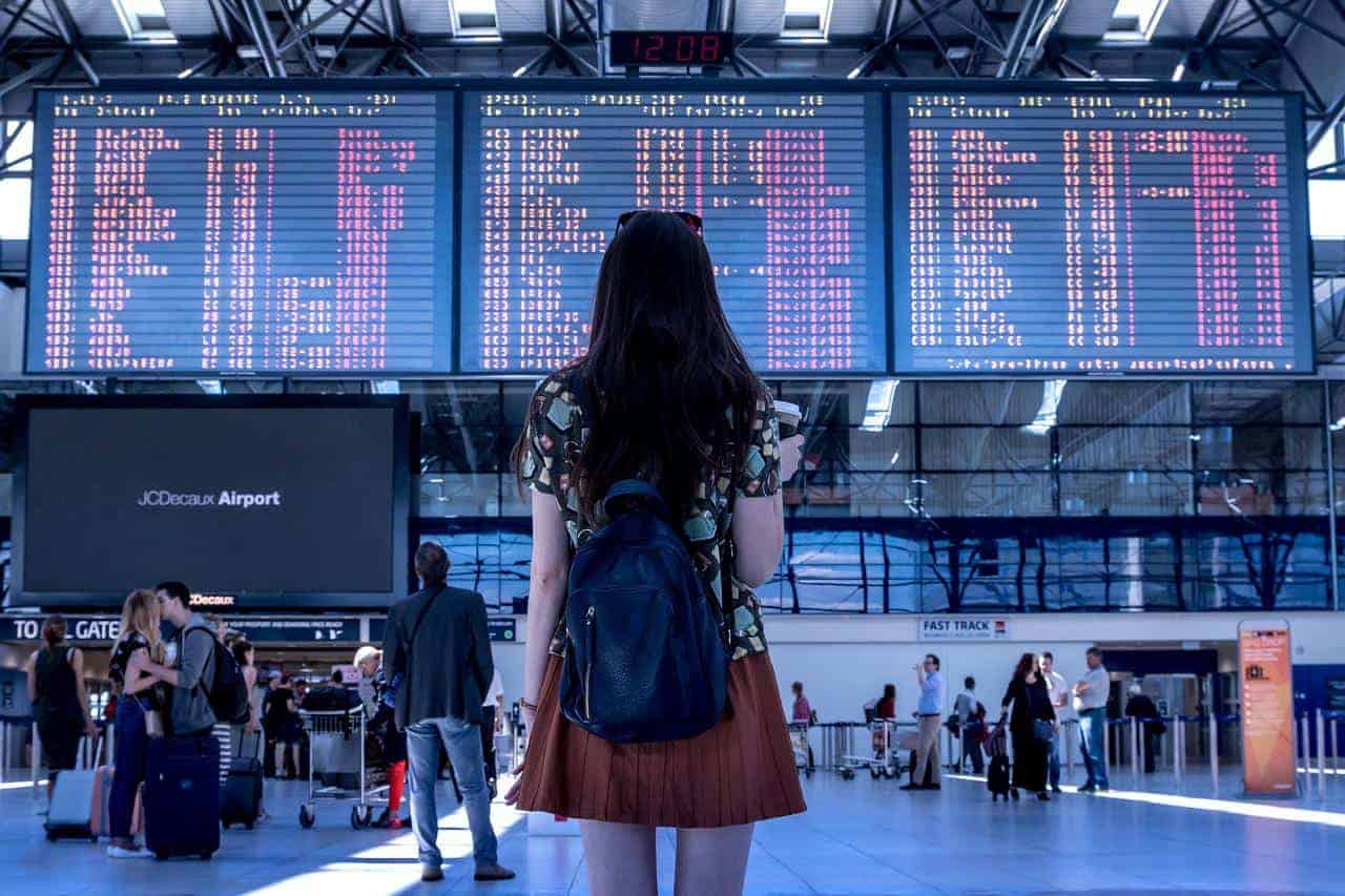 A woman wearing a backpack and looking at a flight board