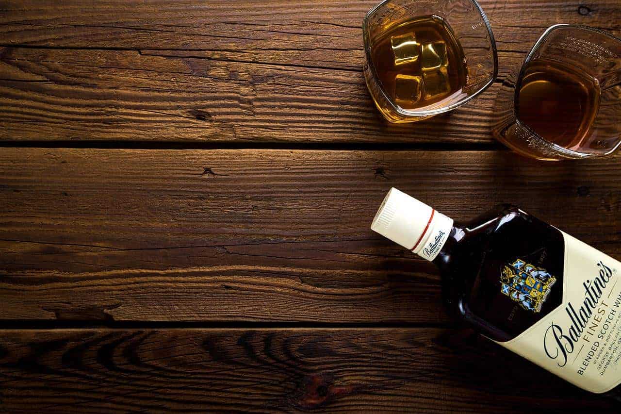 An opened bottle and glass of scotch alcohol on a wooden table
