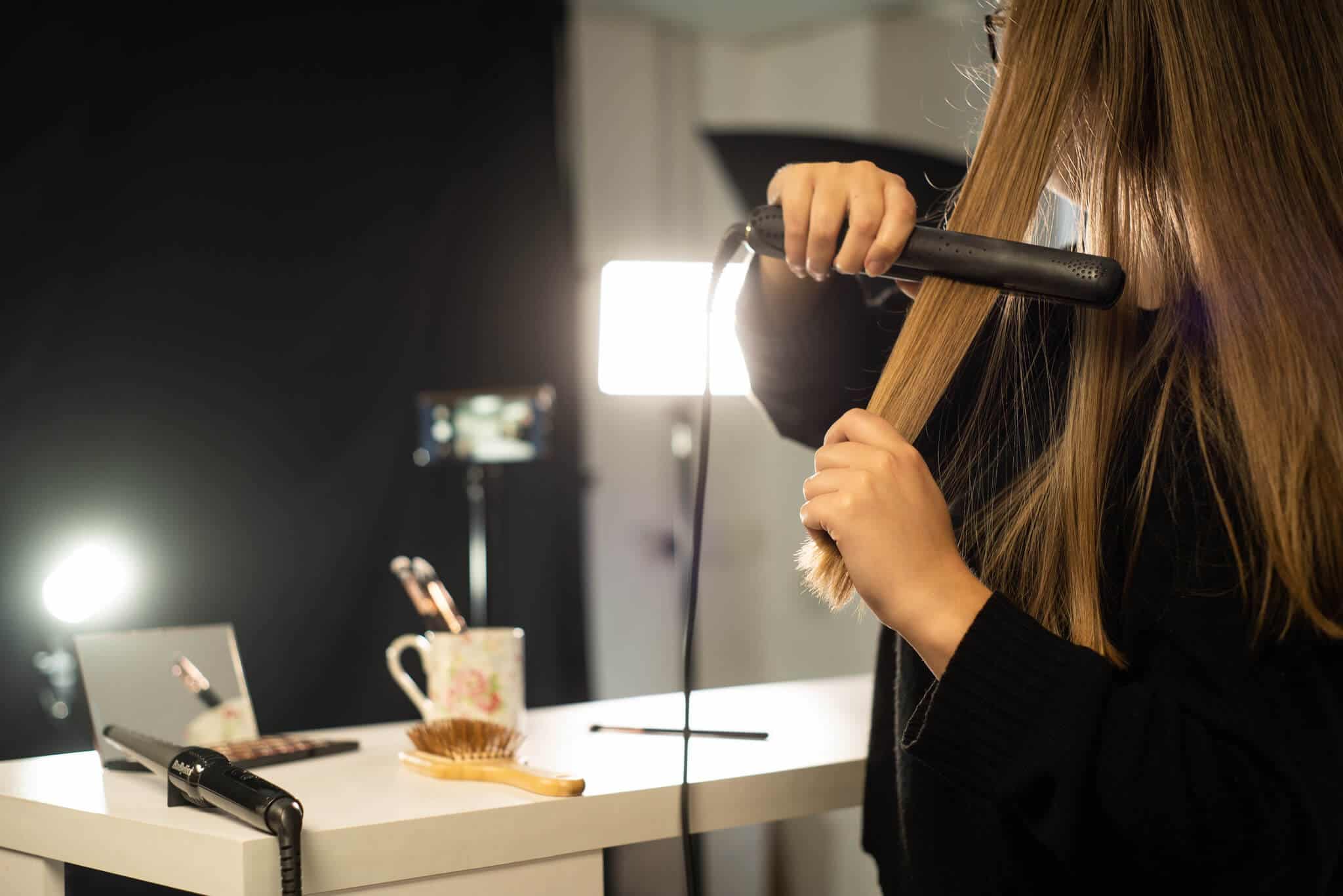 A woman straightening her hair in front of a mirror