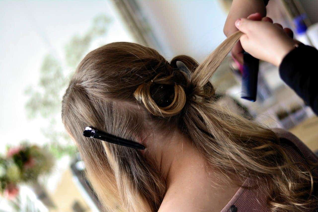 A hairdresser using a curling iron on a woman with light brown hair