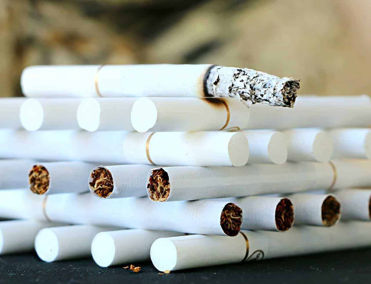 A lit cigarette laying and onto of stacked cigarettes