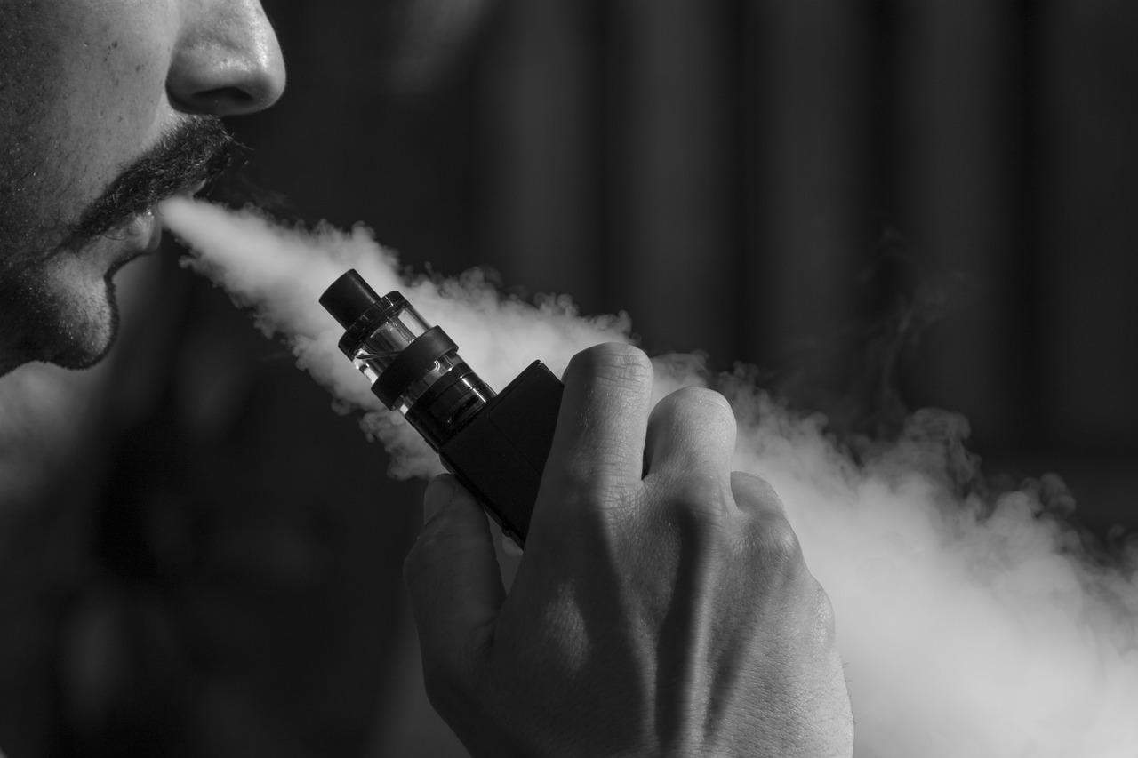 A man using a vape and blowing a vape cloud