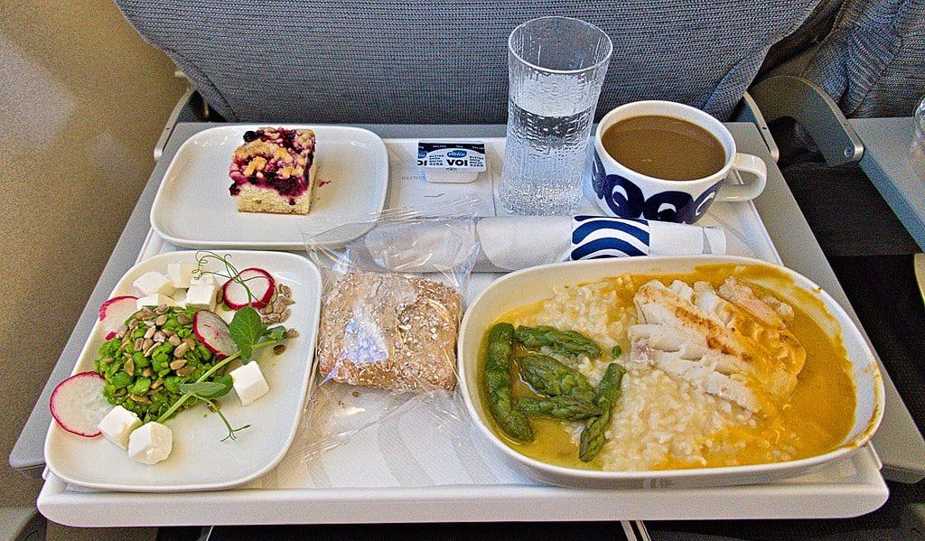 Airplane food meal containing chicken, a salad, bread, and a pastry