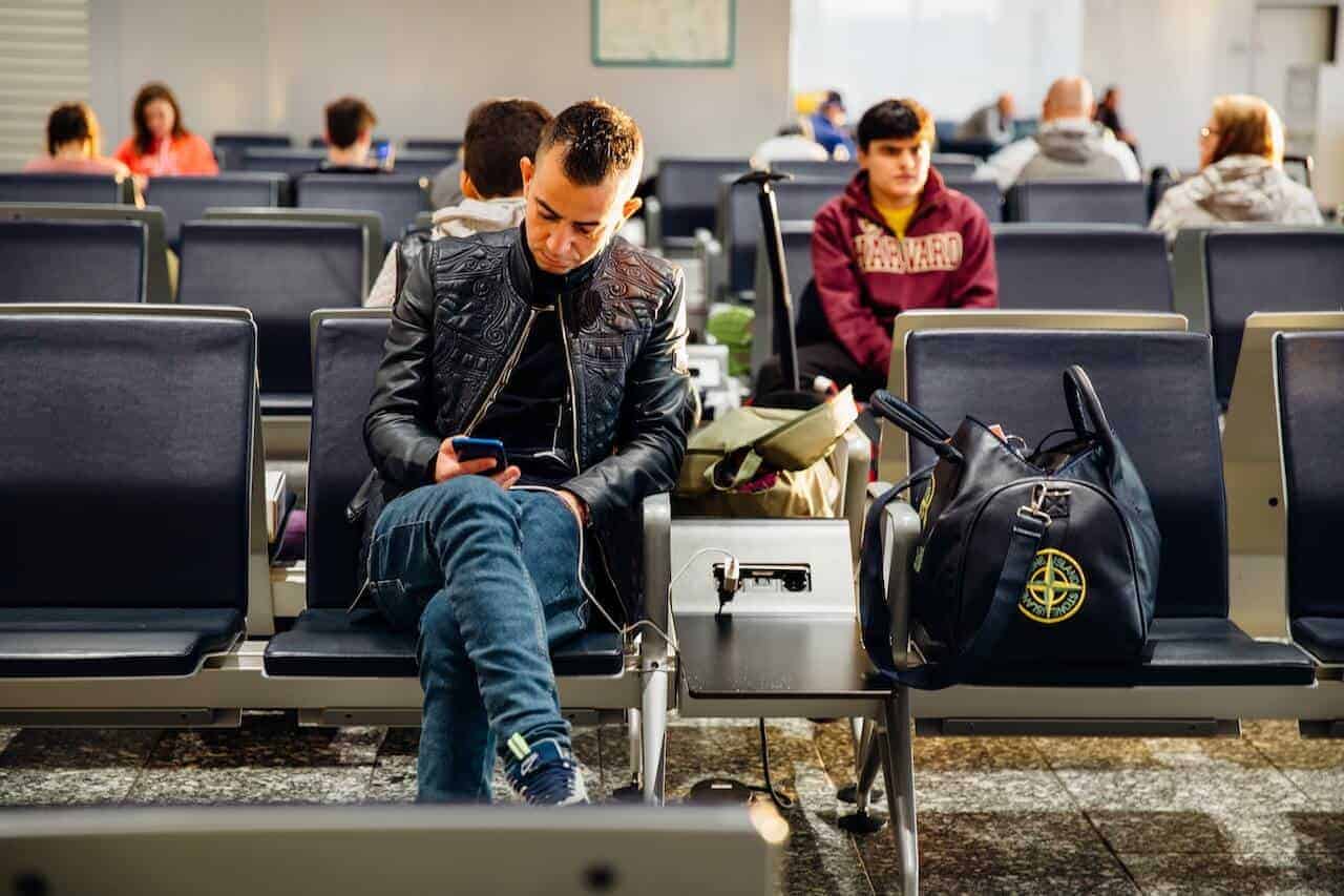 man sitting at the airport with his carry on bag and reading
