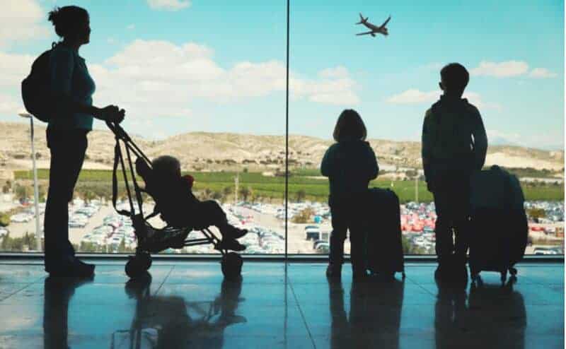 A mom with her 3 kids watching at the airport watching a plane take off