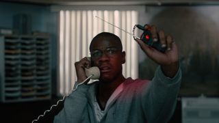 A still from the movie Breaking in which John Boyega's character Lance Corporal Brian Brown-Easley is holding a phone and a small device