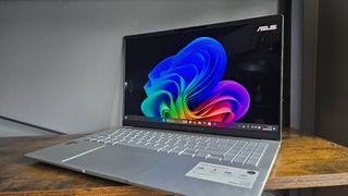 The Asus Vivobook S 15 Copilot+ in silver pictured on a wooden desk.