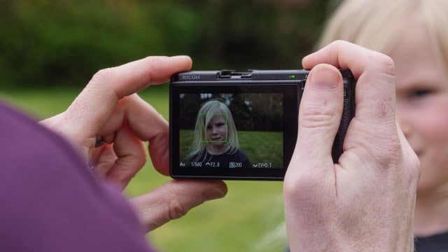 A hand holding the Ricoh GR IIIx camera