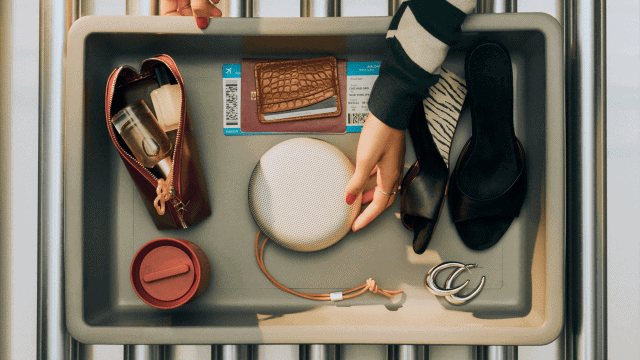The Bang & Olufsen A1 3rd Gen on an airport security tray, along with other travel items