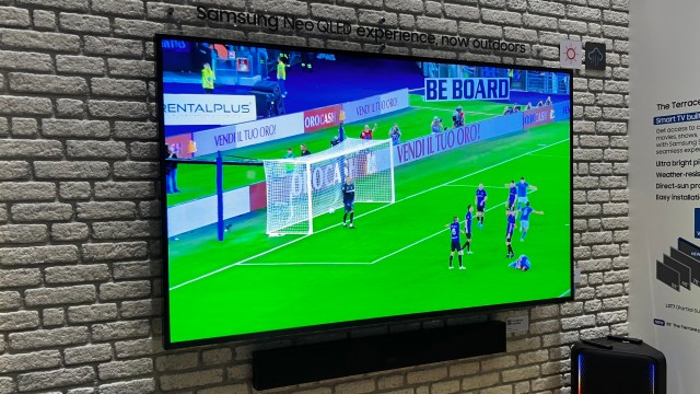 The Samsung Terrace TV on a brick-style wall, with a football match on the screen