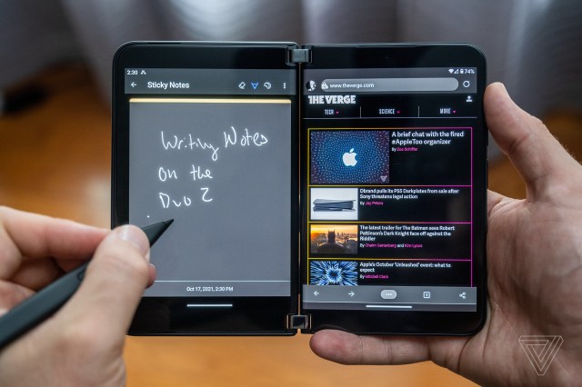 A person writing on the Surface Duo 2’s left screen with the Microsoft Surface Slim Pen 2 while reading a website displayed on the right screen.