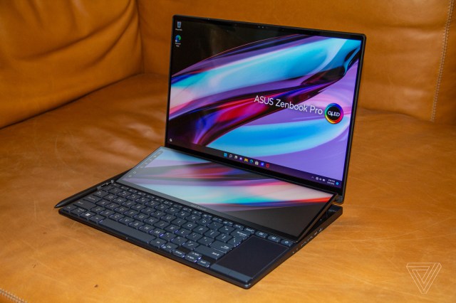 The Asus Zenbook Pro 14 Duo angled to the left side on a brown couch. Both screens display a multicolor background with the Asus Zenbook Pro OLED logo.