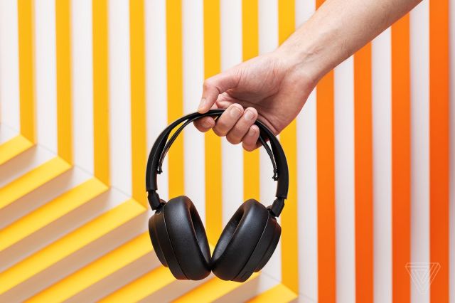 A picture of a hand holding up the black headset, on a background of orange and yellow stripes set in a geometric pattern.