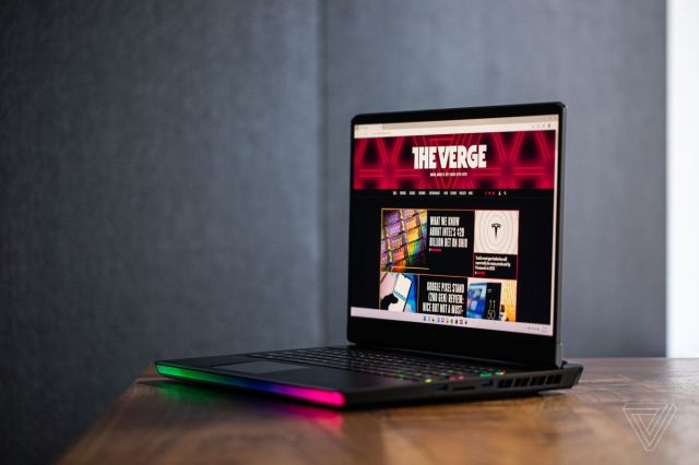 The MSI GE76 Raider open on a wooden table seen from the right. The screen displays The Verge homepage.