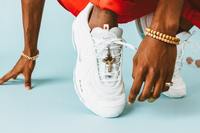 A person wears Nike sneakers with a cross hanging from the tie.