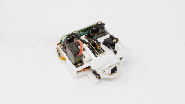 Pieces of hardware and circuitry assembled in a square, at the bottom is what looks like plastic eyelids on hinges. 