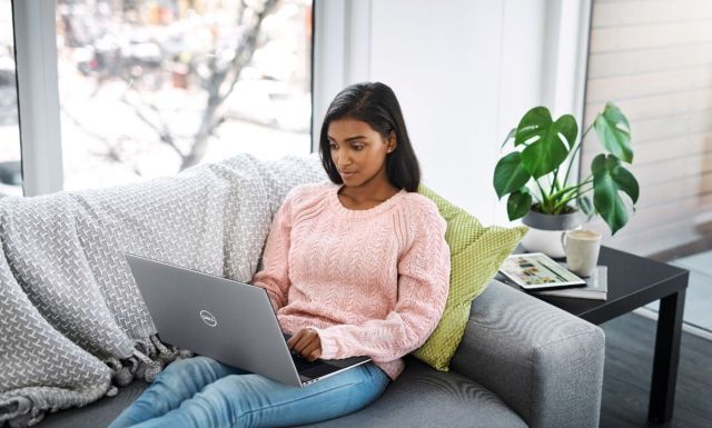 A user types on the Dell XPS 17 while seated on a couch in a living room setting.