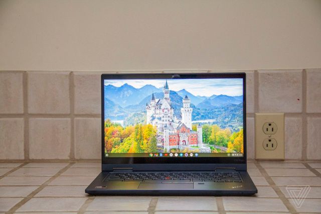 The Lenovo ThinkPad C13 Yoga Chromebook seen from the front on a tile counter. The screen displays a white castle surrounded by trees with mountains in the background.