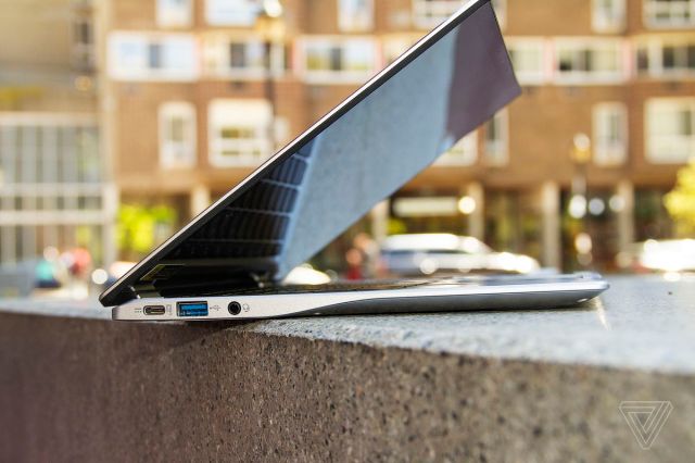 The Acer Chromebook Spin 513 seen from the left, half open, on a stone bench. An apartment building is in the background.