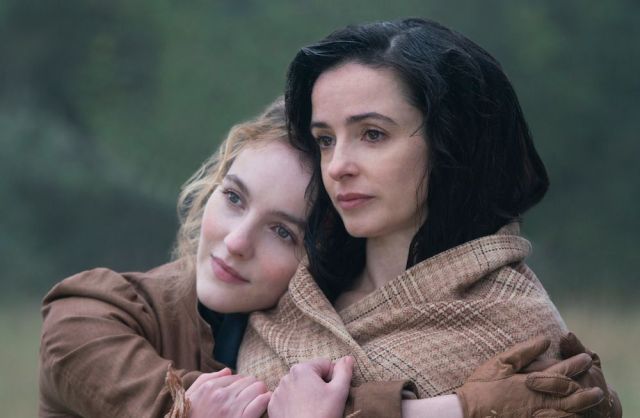 Two women in 19th century clothes embrace.