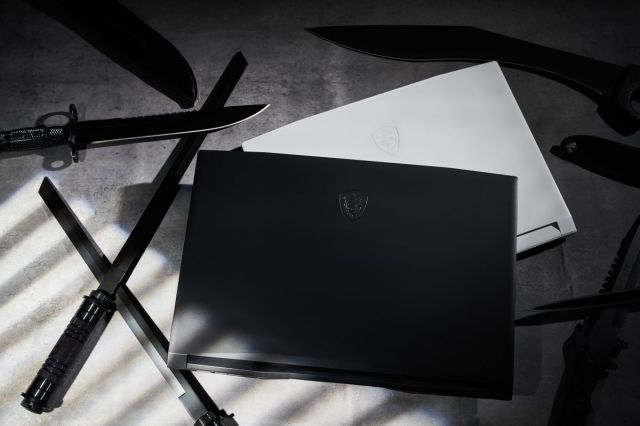 The MSI GF76 Katana and GF66 Katana, closed, stacked on top of each other, seen from above, in black and white colors respectively. Swords, katanas, and other weapons surround them on the floor.