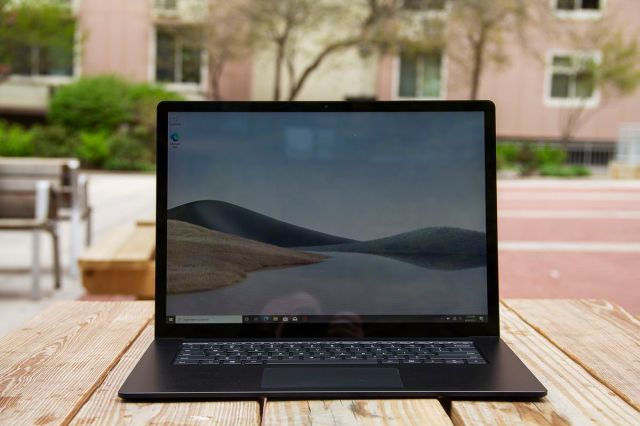 The Surface Laptop 4 15-inch open on a picnic table with a pink apartment building in the background. The screen displays sand dunes with a blue sky.
