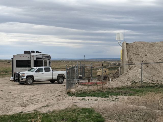 A photo of a white truck and tan camper van parked outside a bunker surrounded by a wire fence.