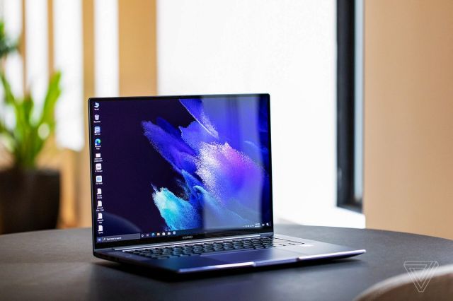 The Huawei MateBook 16 on a table with a potted plant in the background, angled to the right, open. The screen displays a blue and purple background.