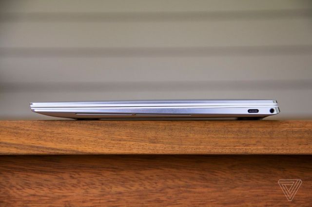 The Dell XPS 13 OLED closed seen from the left side on a wooden table.