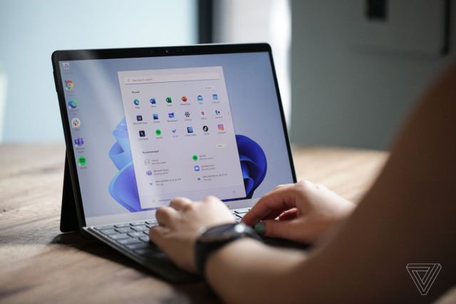 A user types on the Surface Pro 8 from behind. The screen displays the Windows 11 start menu on a white and blue background.