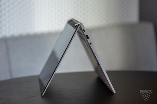 The Asus Chromebook Flip CX5 in tent mode, seen from the left side on a black table with a gray fabric bench in the background.