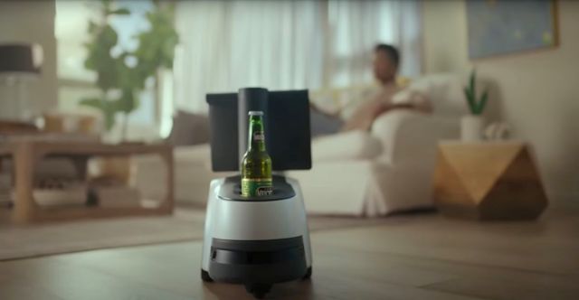 A view of the Astro robot approaching a woman. A beer rests in its cupholder.